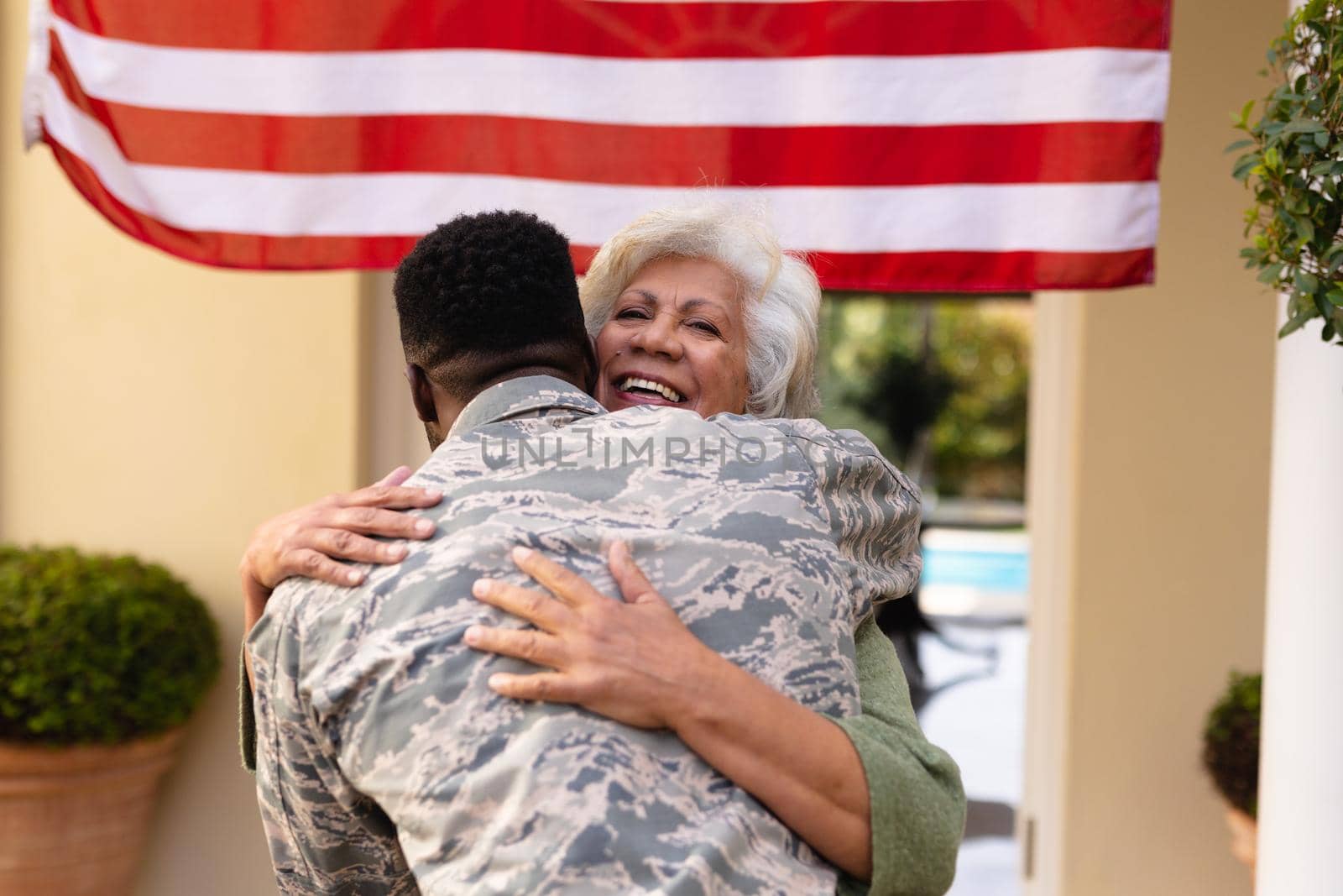 Happy senior african american woman embracing soldier son on his return home at entrance. family, bonding and patriotism, unaltered.