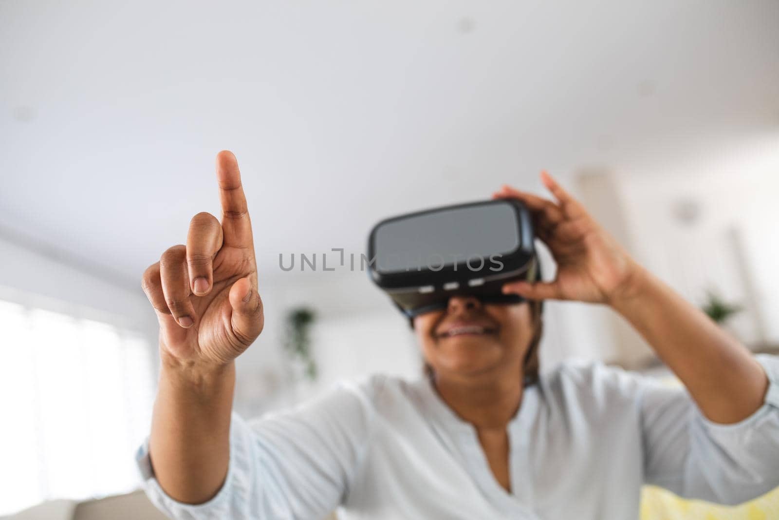 African american senior woman pointing while wearing virtual reality simulator at home, copy space. lifestyle, futuristic and modern technology.