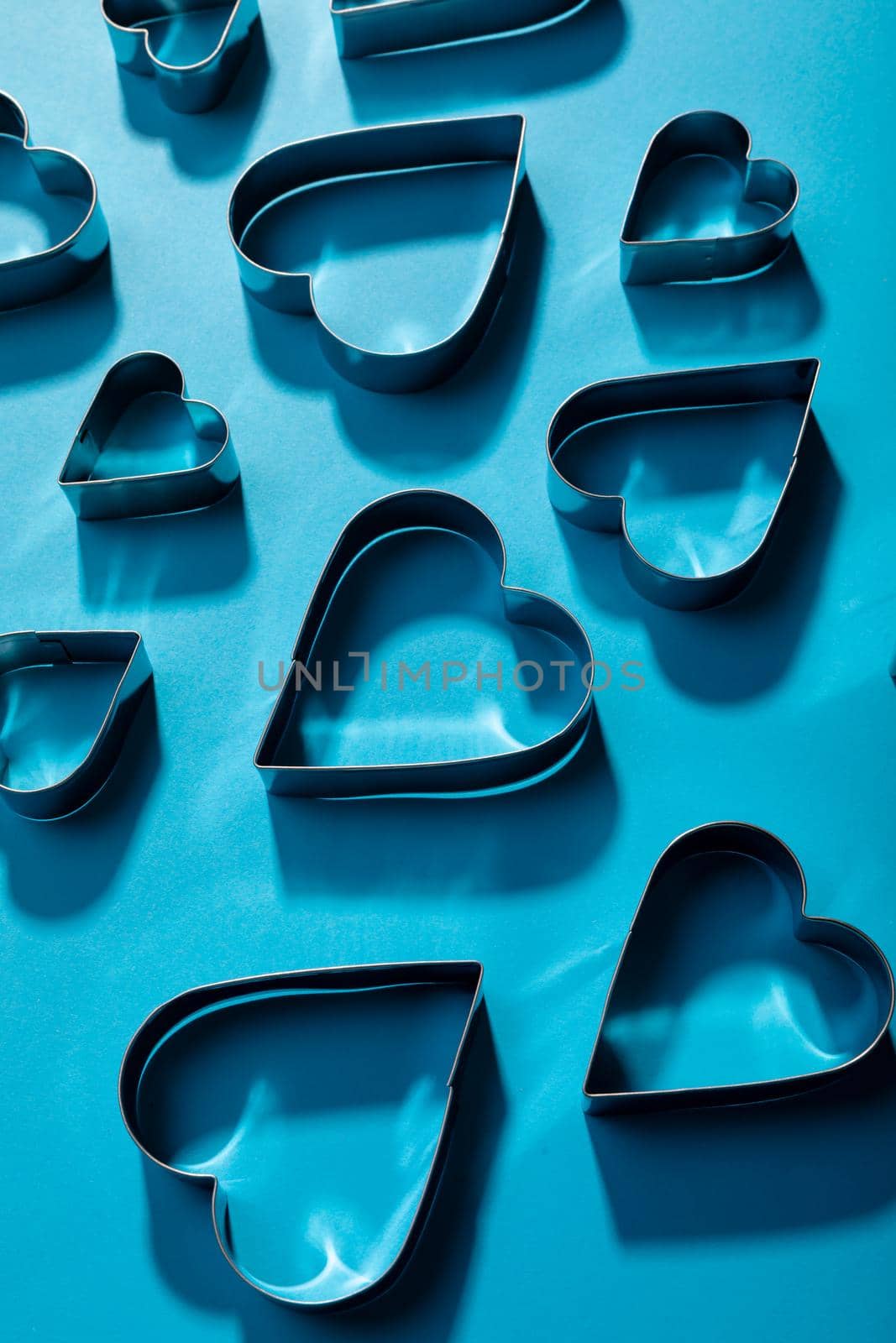 High angle view of heart shape pastry cutters with shadows on blue background. valentine and copy space.