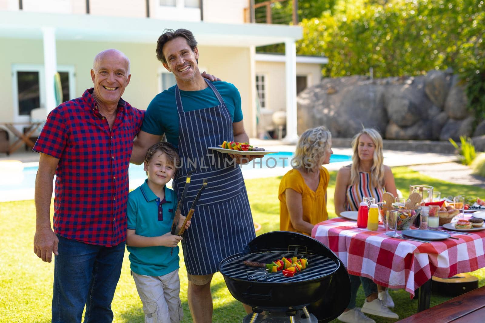 Portrait of caucasian grandfather, father and son barbecuing in the garden by Wavebreakmedia