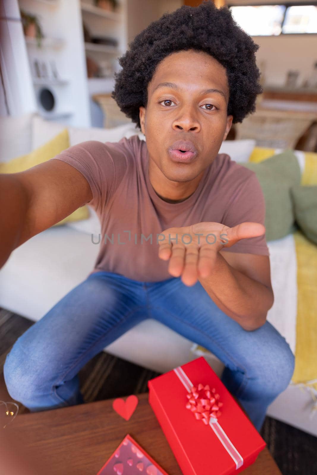 Portrait of african american young man blowing kiss during video call while sitting at home. unaltered, online dating, video call, love, lifestyle and distant valentine day celebration.