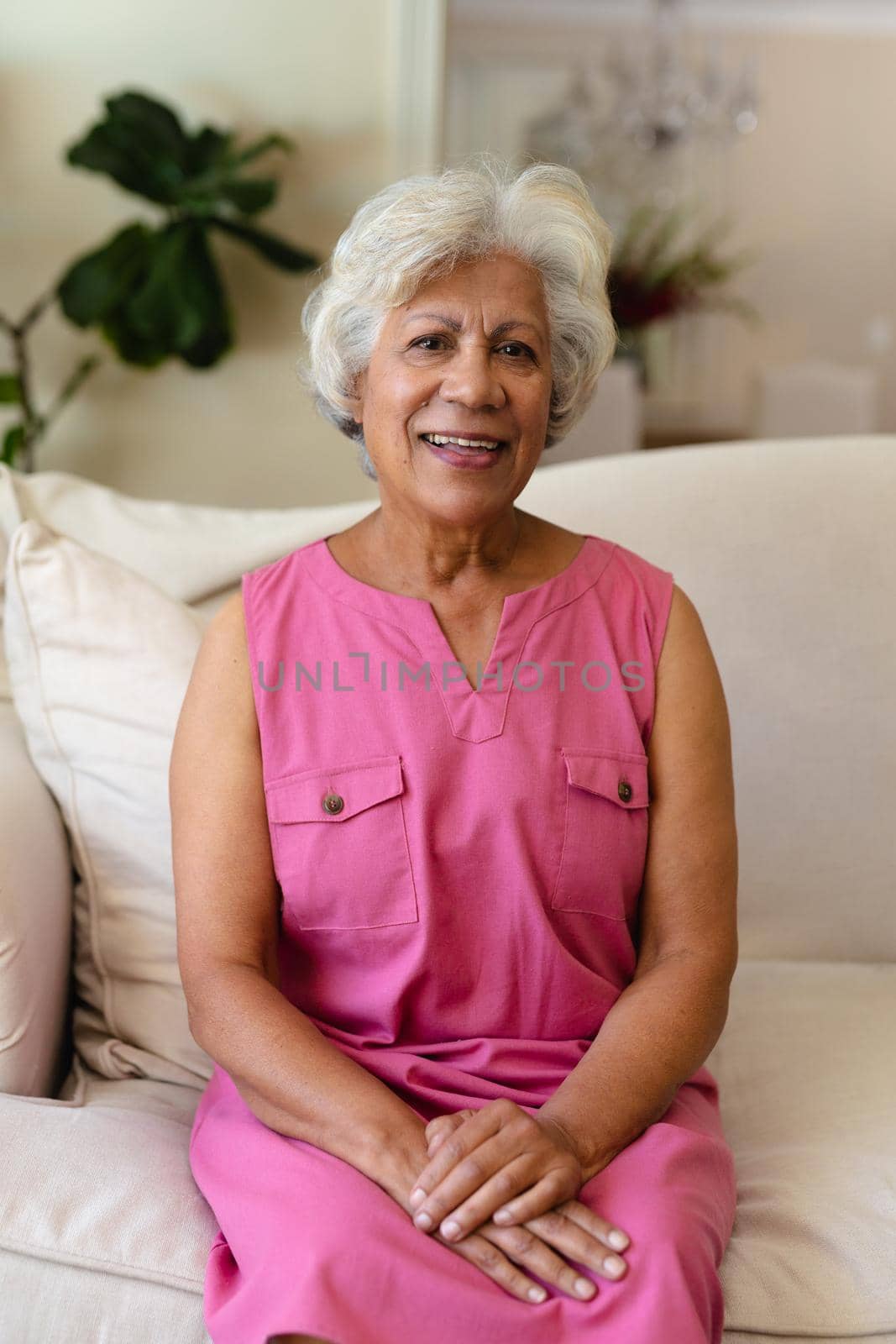 Portrait of smiling biracial mature woman with gray hair sitting on sofa at home by Wavebreakmedia
