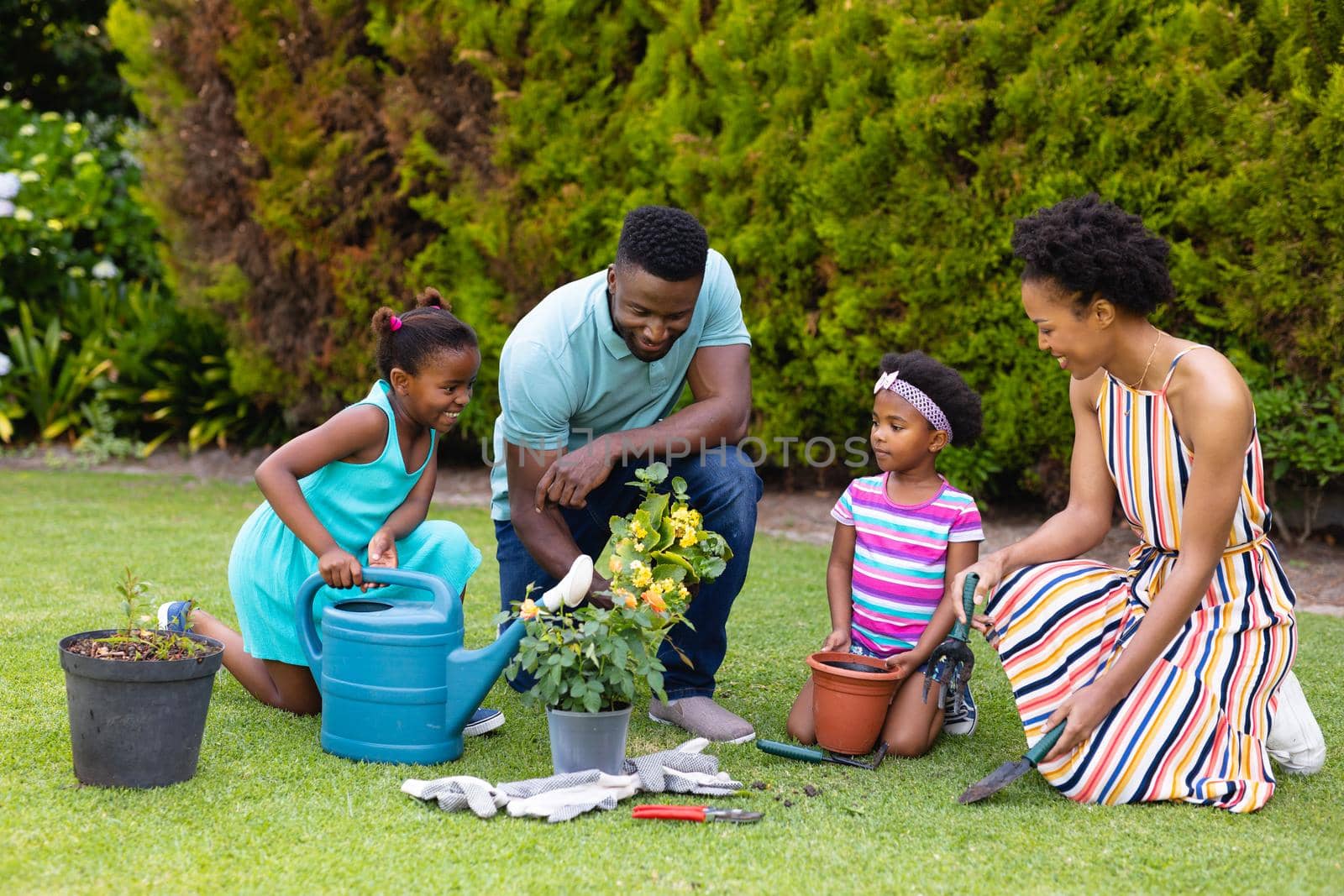 African american family watering the plants together in the garden. family, love and togetherness concept, unaltered.