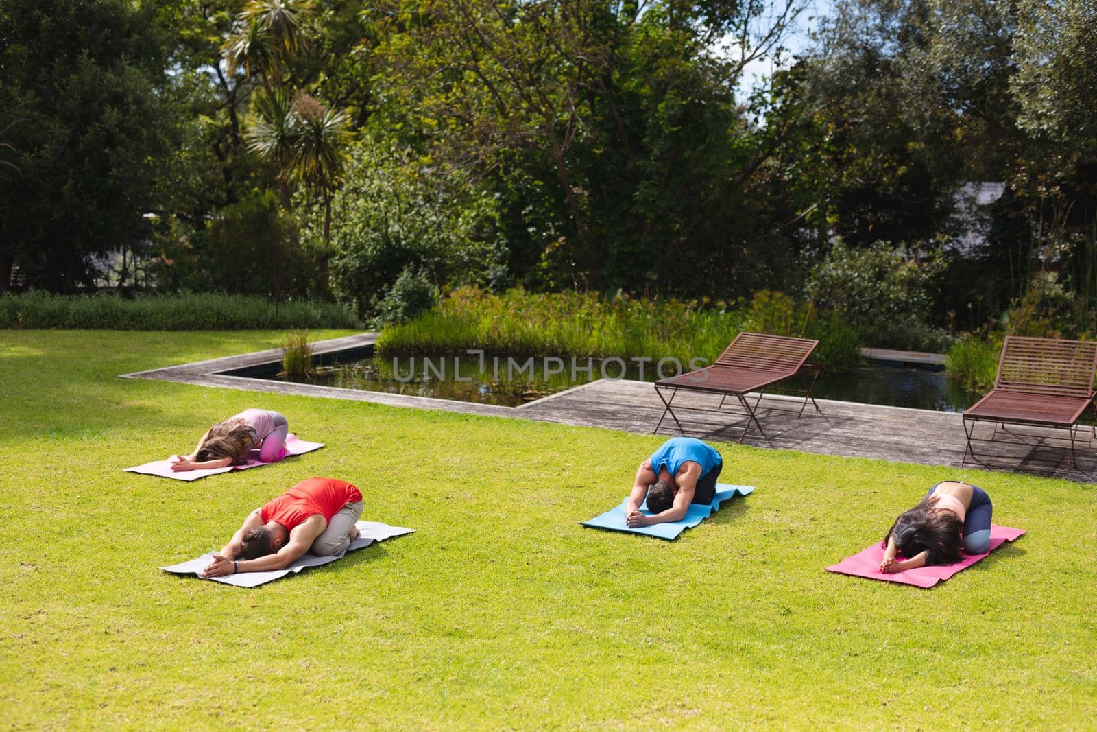 Men and women practicing yoga on exercise mats in public park on sunny day. healthy lifestyle and body care.