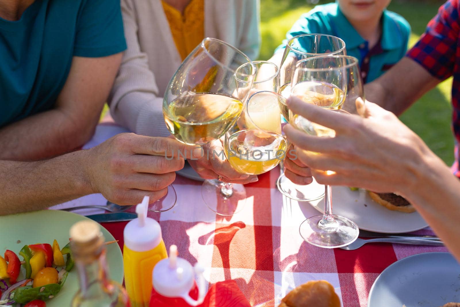 Midsection of caucasian family toasting drinks at table in garden. family, togetherness and weekend lifestyle concept, unaltered.