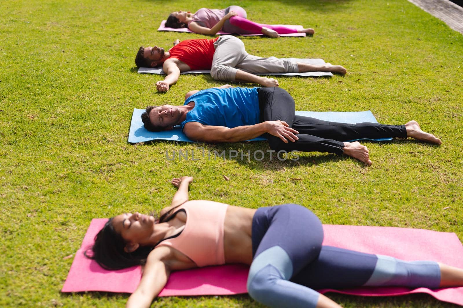 Women and men practicing yoga while lying on exercise mat in park by Wavebreakmedia