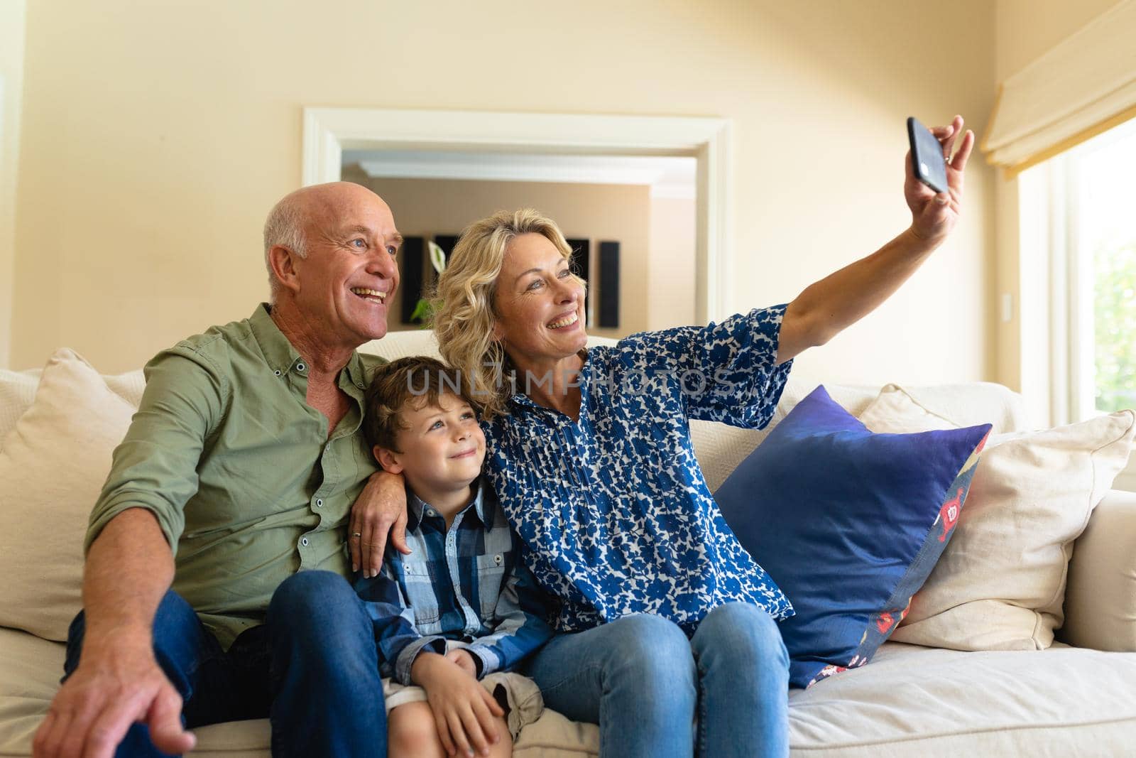 Caucasian grandparents and grandson taking a selfie while sitting together on couch at home. family, love and togetherness concept, unaltered.