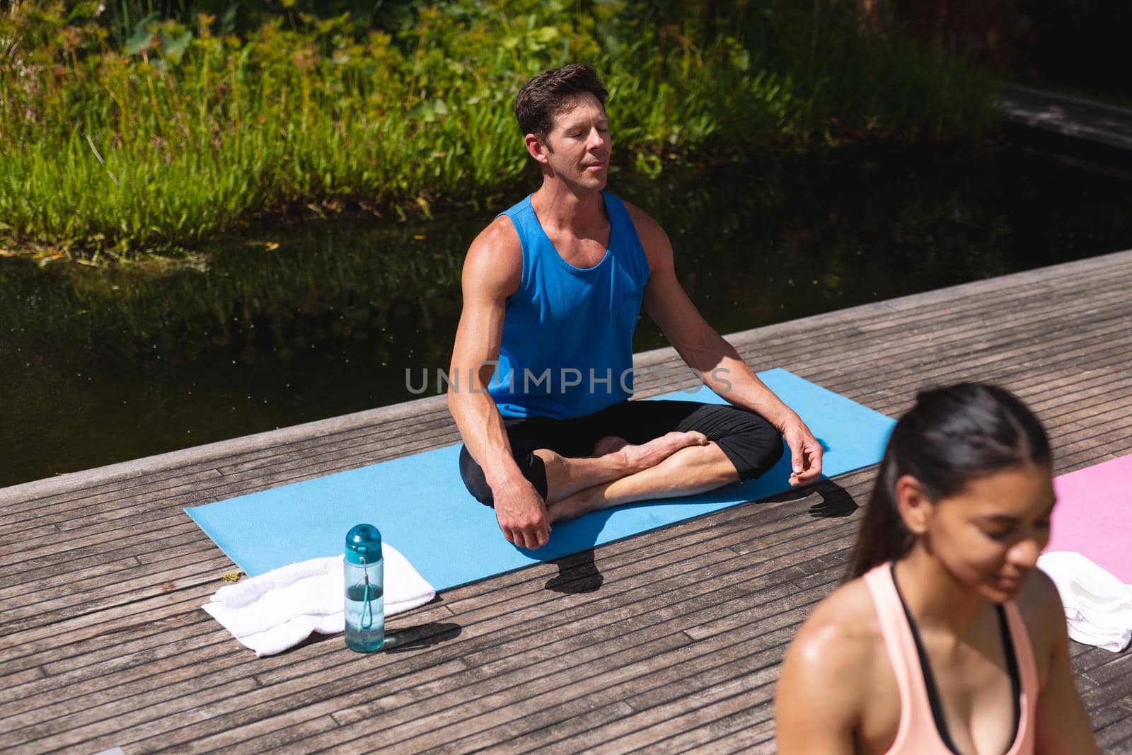 Man in sportswear practicing meditation while sitting on exercise mat in park by Wavebreakmedia