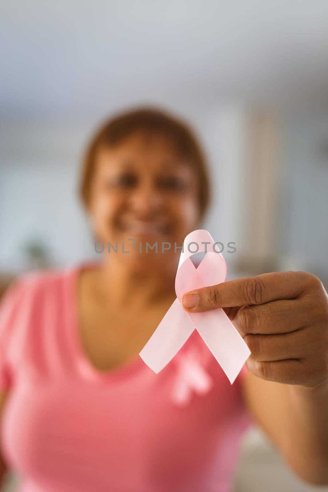 Smiling senior woman showing pink ribbon representing breast cancer awareness by Wavebreakmedia