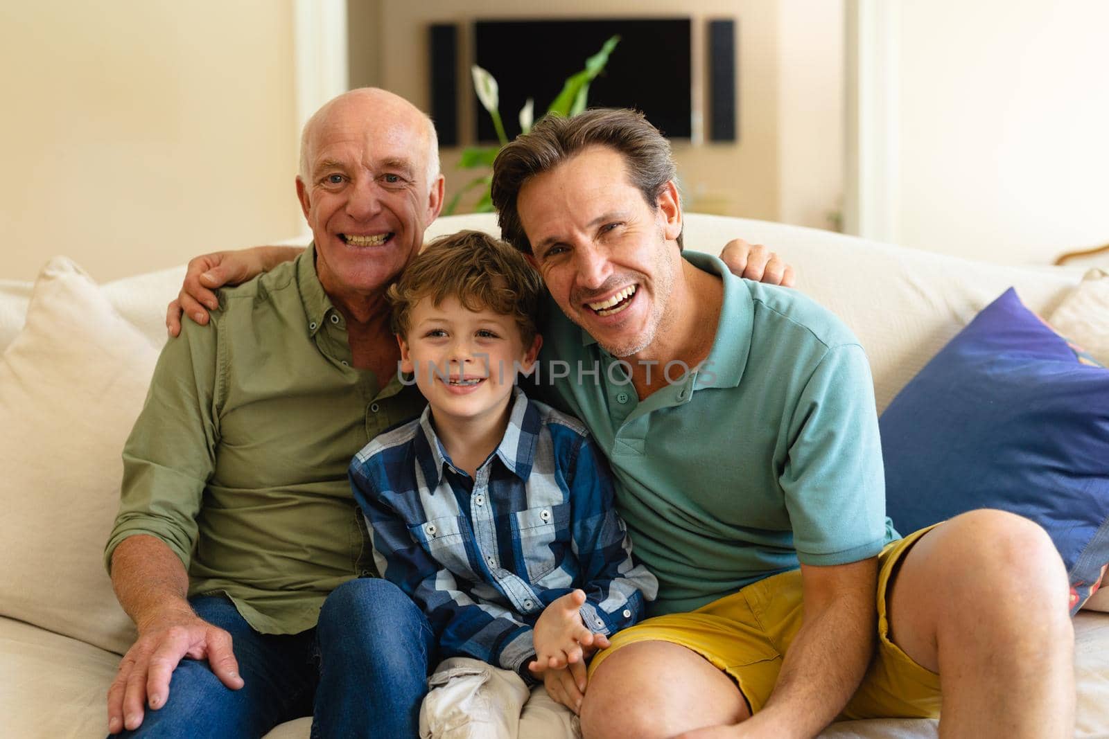 Portrait of caucasian grandfather, father and son smiling while sitting together on couch at home. family, love and togetherness concept, unaltered.