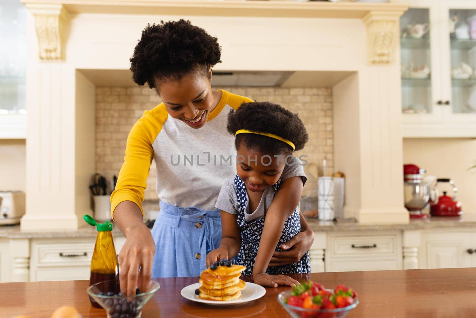 African american mother putting berries over the pancake of her daughter in the kitchen at home by Wavebreakmedia