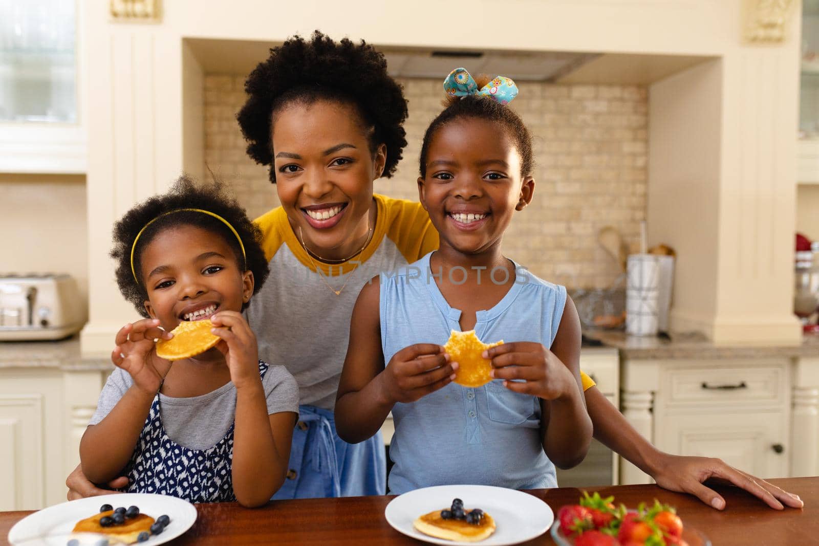 Portrait of african american mother and her two daughters having breakfast in kitchen at home by Wavebreakmedia