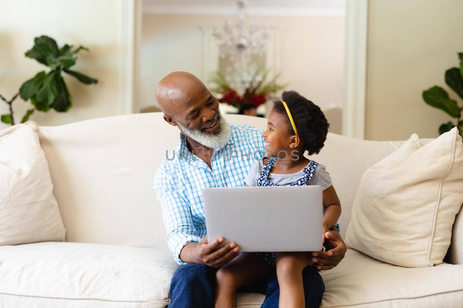 African american grandfather and granddaughter using laptop together sitting on couch at home. family, love and technology concept, unaltered.