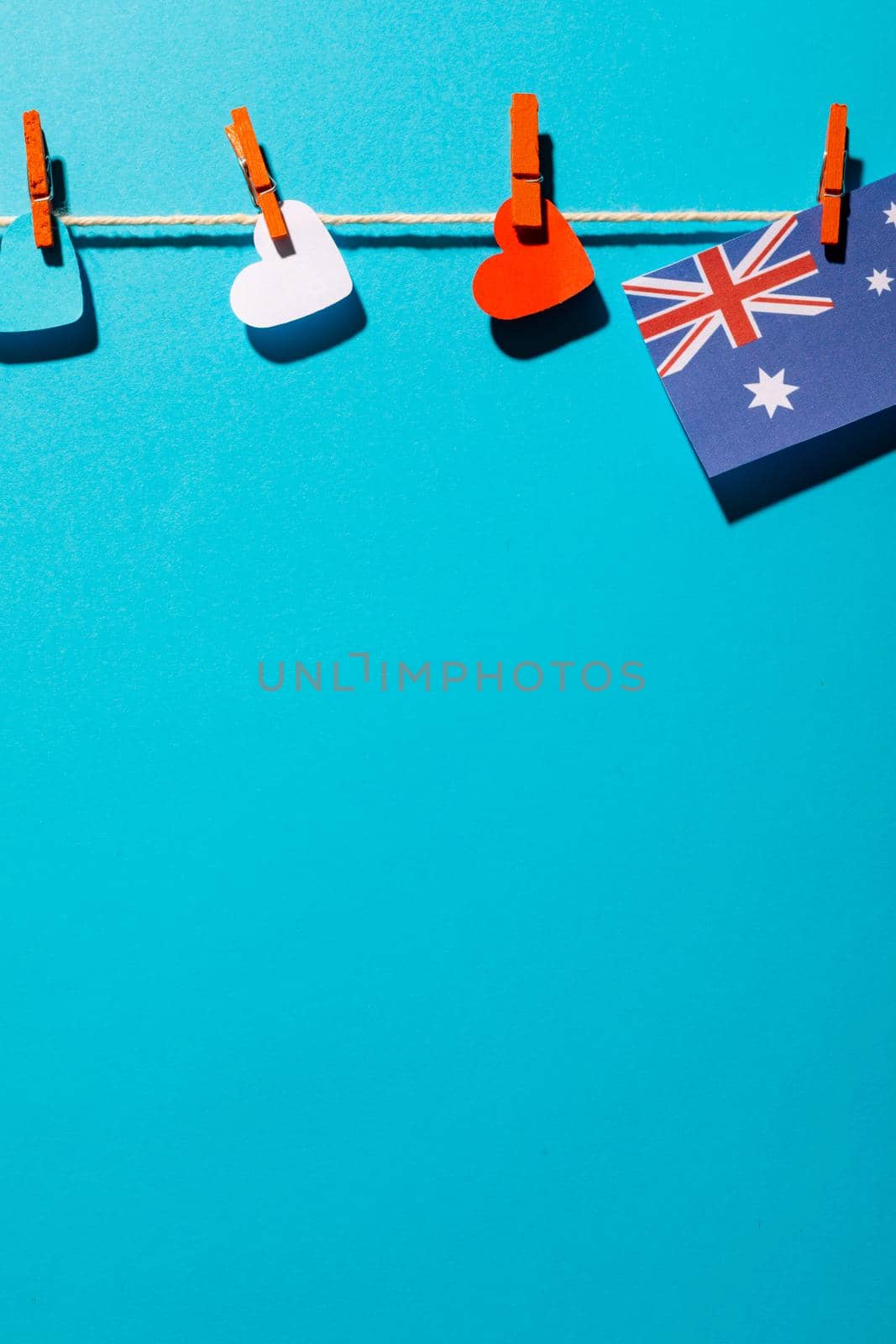 Australia flag and heart shapes hanging on clothesline with copy space over blue background. patriotism, symbol and identity.