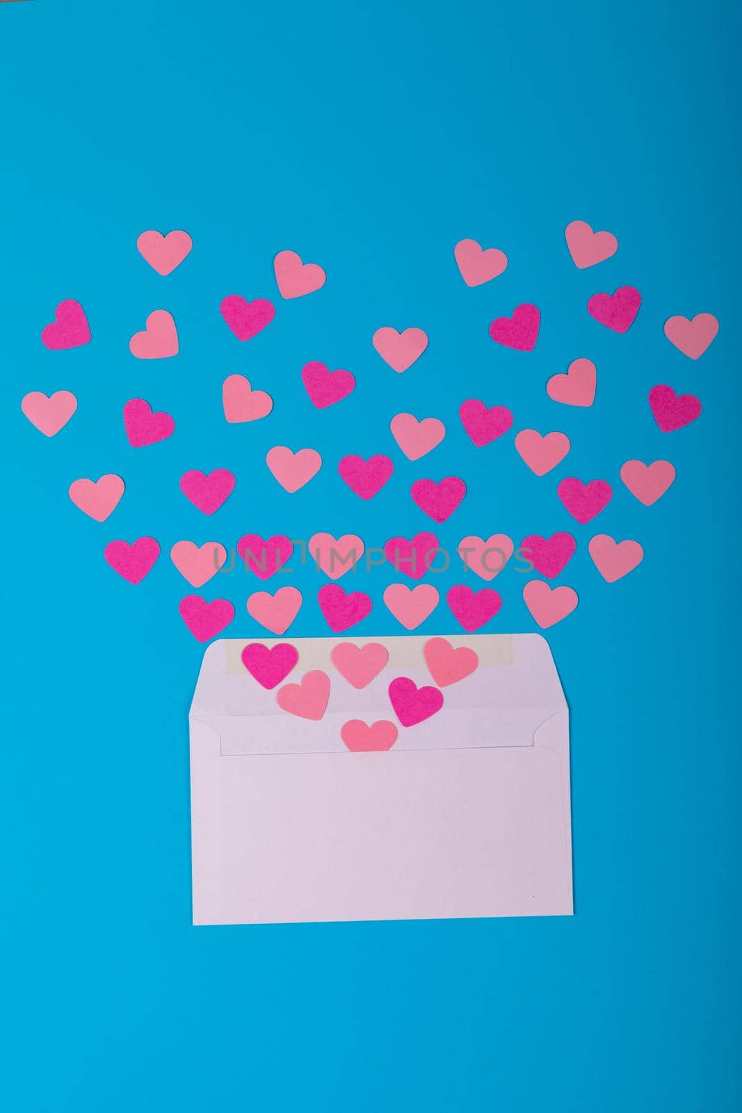 Open white envelope with scattered peach and pink colored heart shapes on blue background. love, valentine present and copy space.