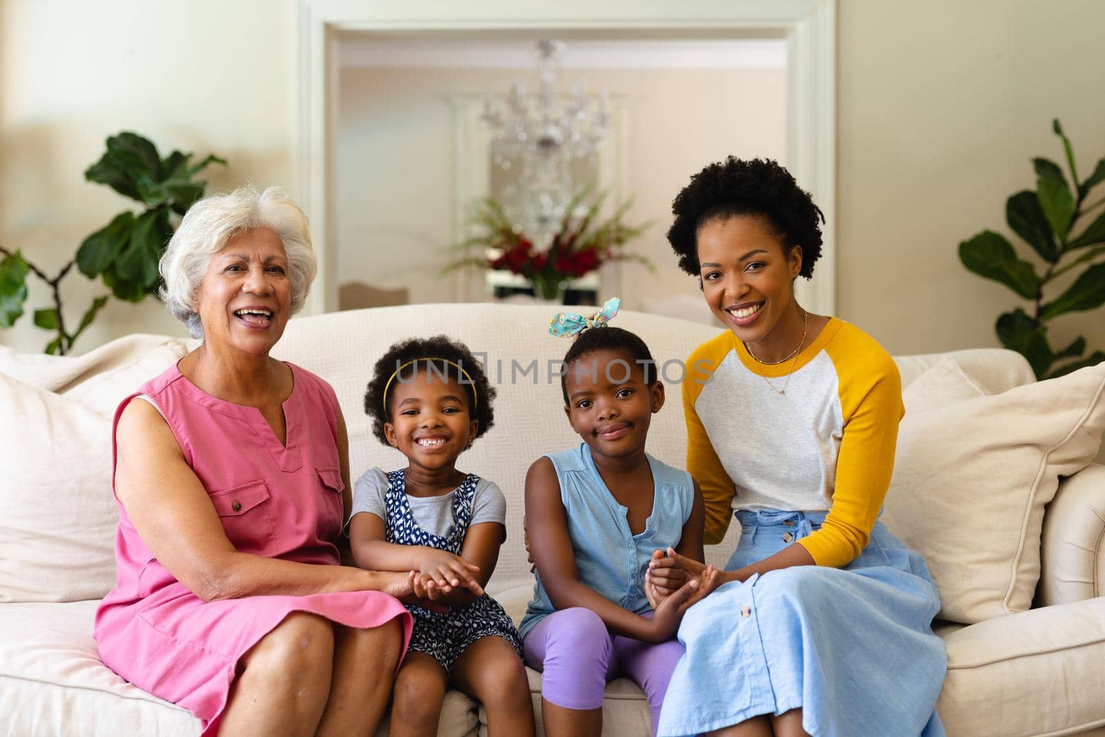 Portrait of african american grandmother, mother and two granddaughters smiling sitting on couch. family, love and togetherness concept, unaltered.
