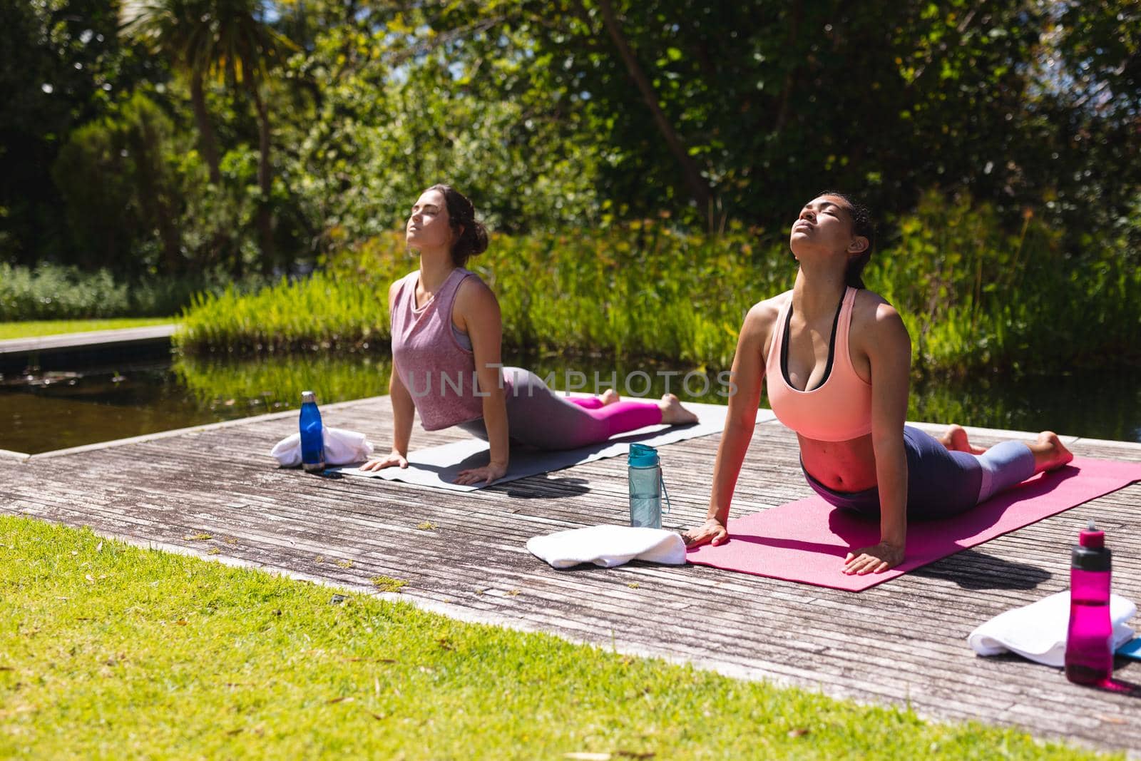 Young women in sportswear practicing yoga on exercise mats at public park by Wavebreakmedia