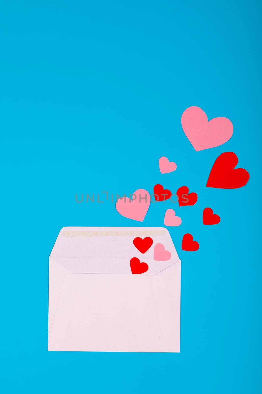 Overhead view of pink and red hearts coming from white envelope on blue background with copy space. valentine's day and love letter concept.