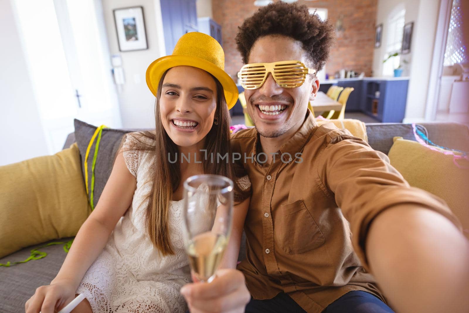 Portrait of happy young biracial couple taking selfie while enjoying party at home by Wavebreakmedia