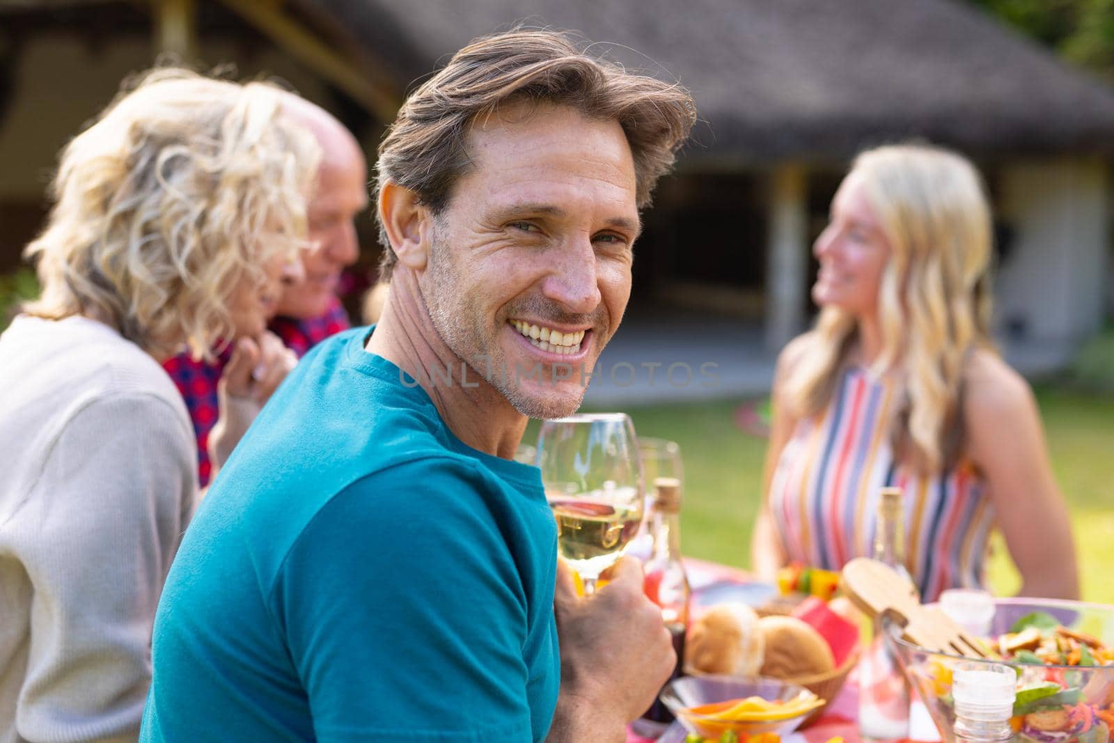Portrait of smiling caucasian man sitting together with family at table in garden. family, togetherness and weekend lifestyle concept, unaltered.