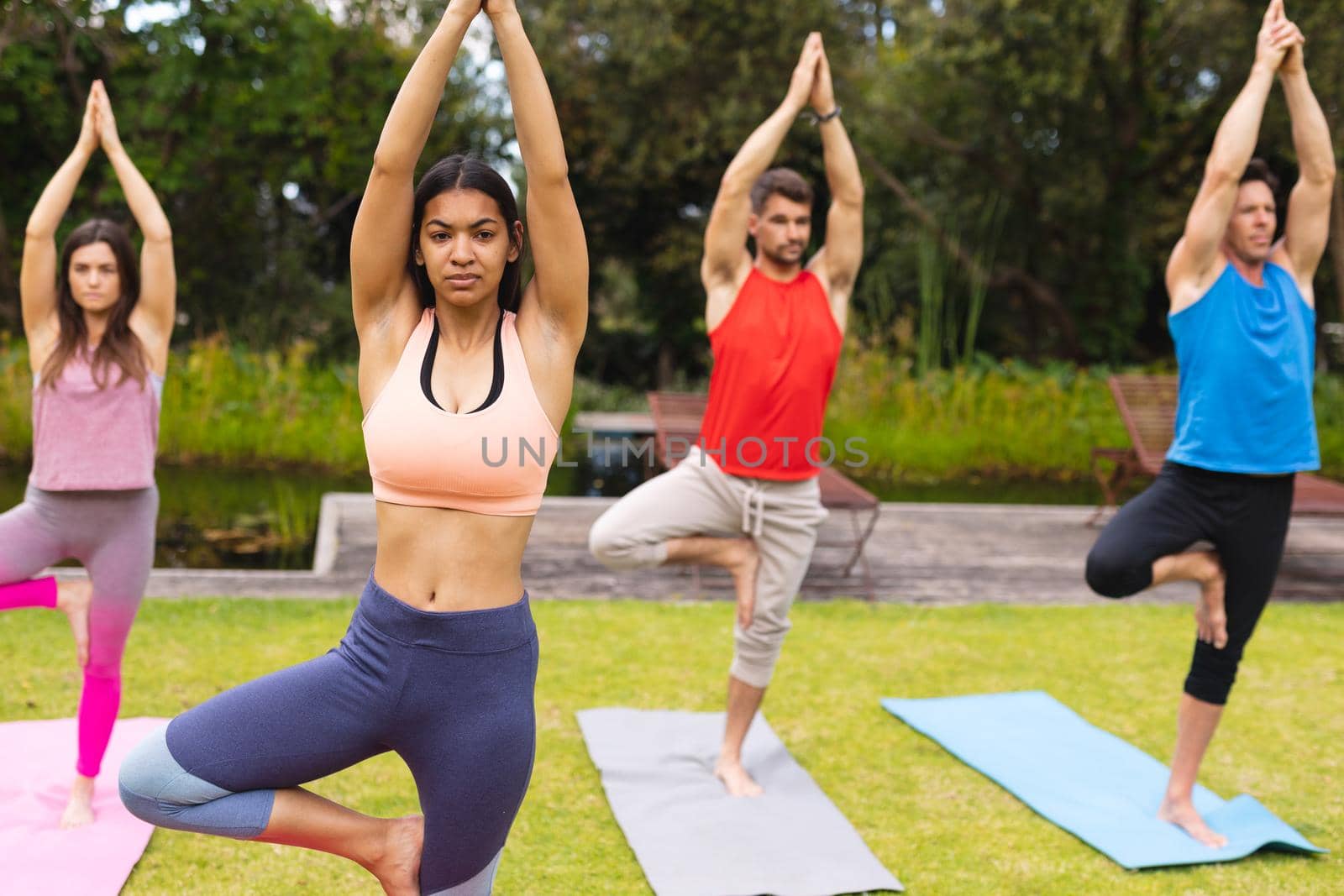Female instructor teaching tree pose to men and woman during yoga session in park. healthy lifestyle and body care.