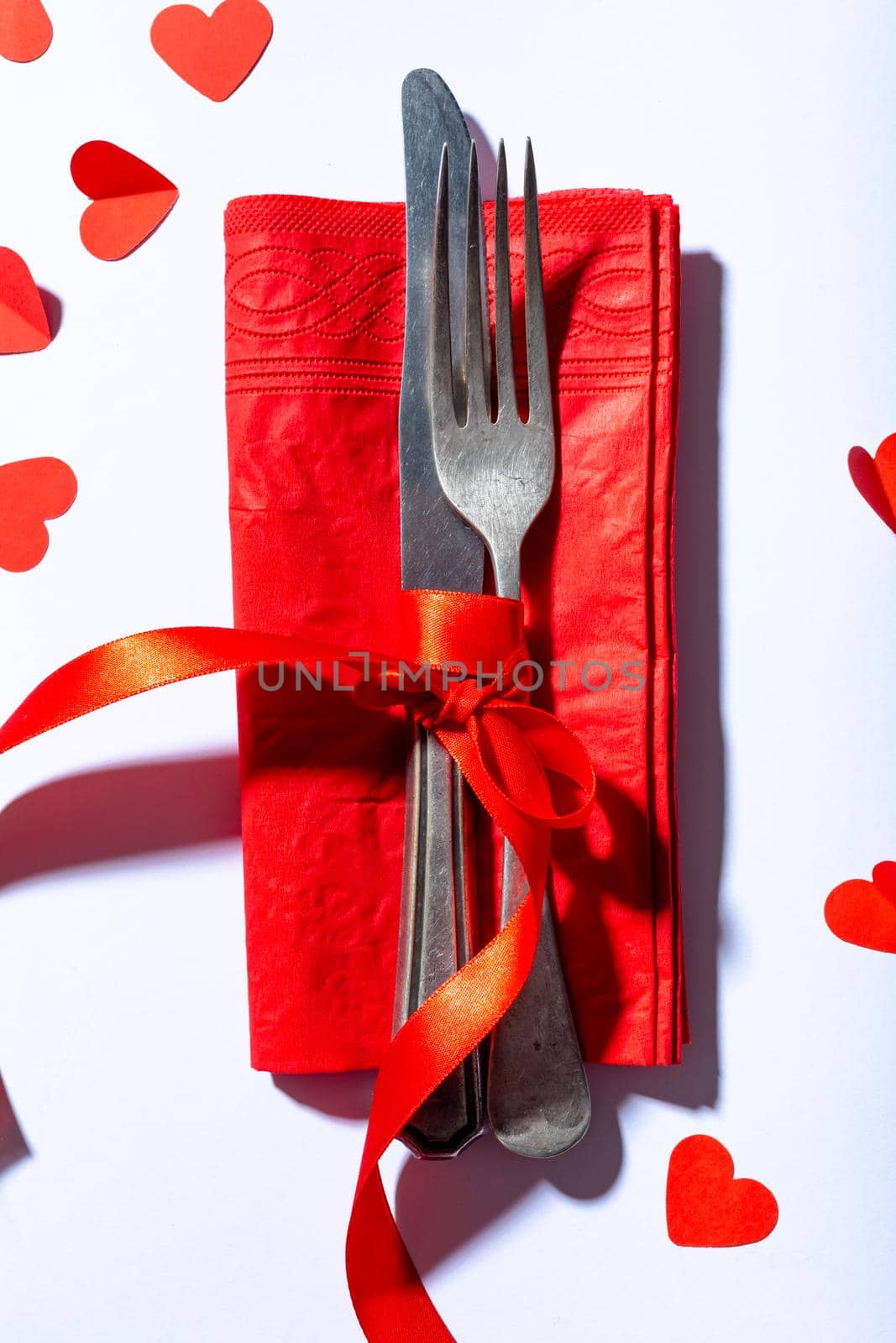 Directly above shot of cutlery tied with ribbon on napkin by hearts on white background, copy space. valentine's day and love concept.