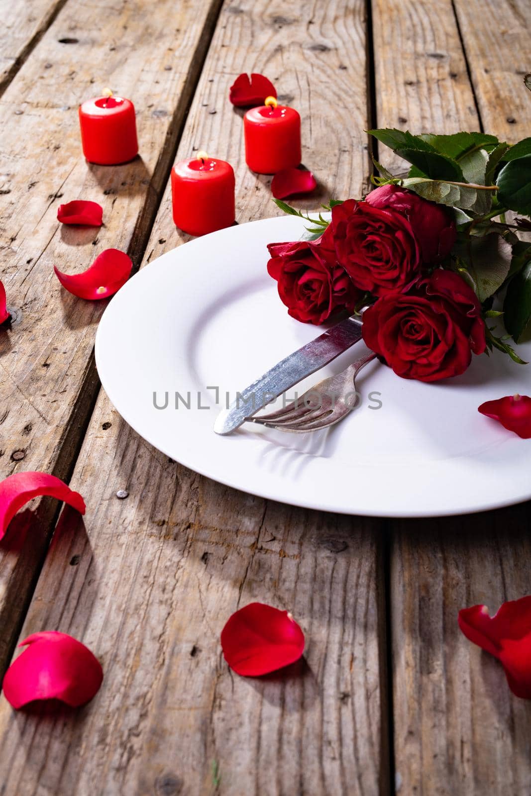 Fresh red roses and cutlery in plate by candles on wooden table, copy space. valentine's day, flower and love concept.