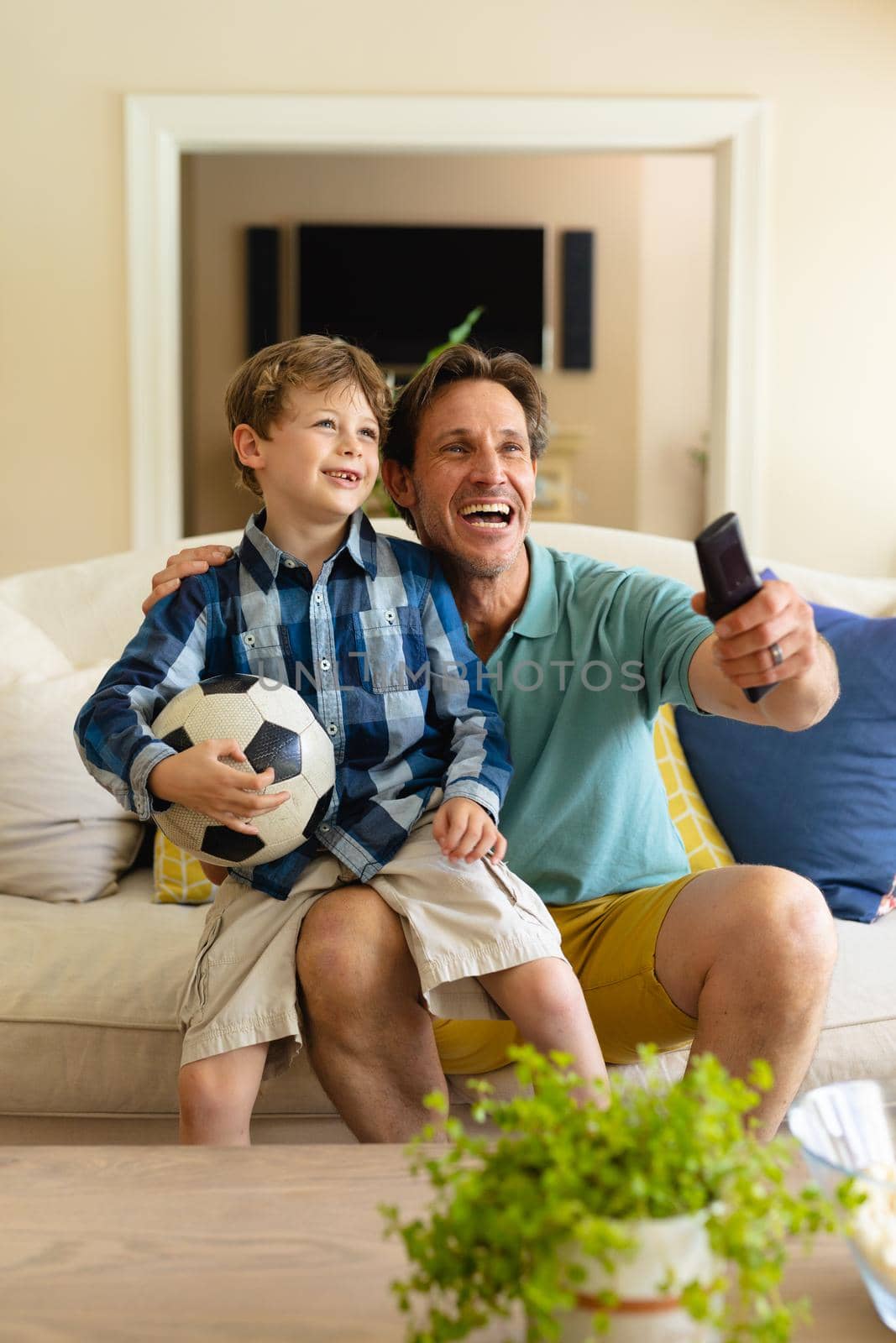 Caucasian father and son watching sports on tv sitting together on the couch at home. sports and entertainment concept, unaltered.