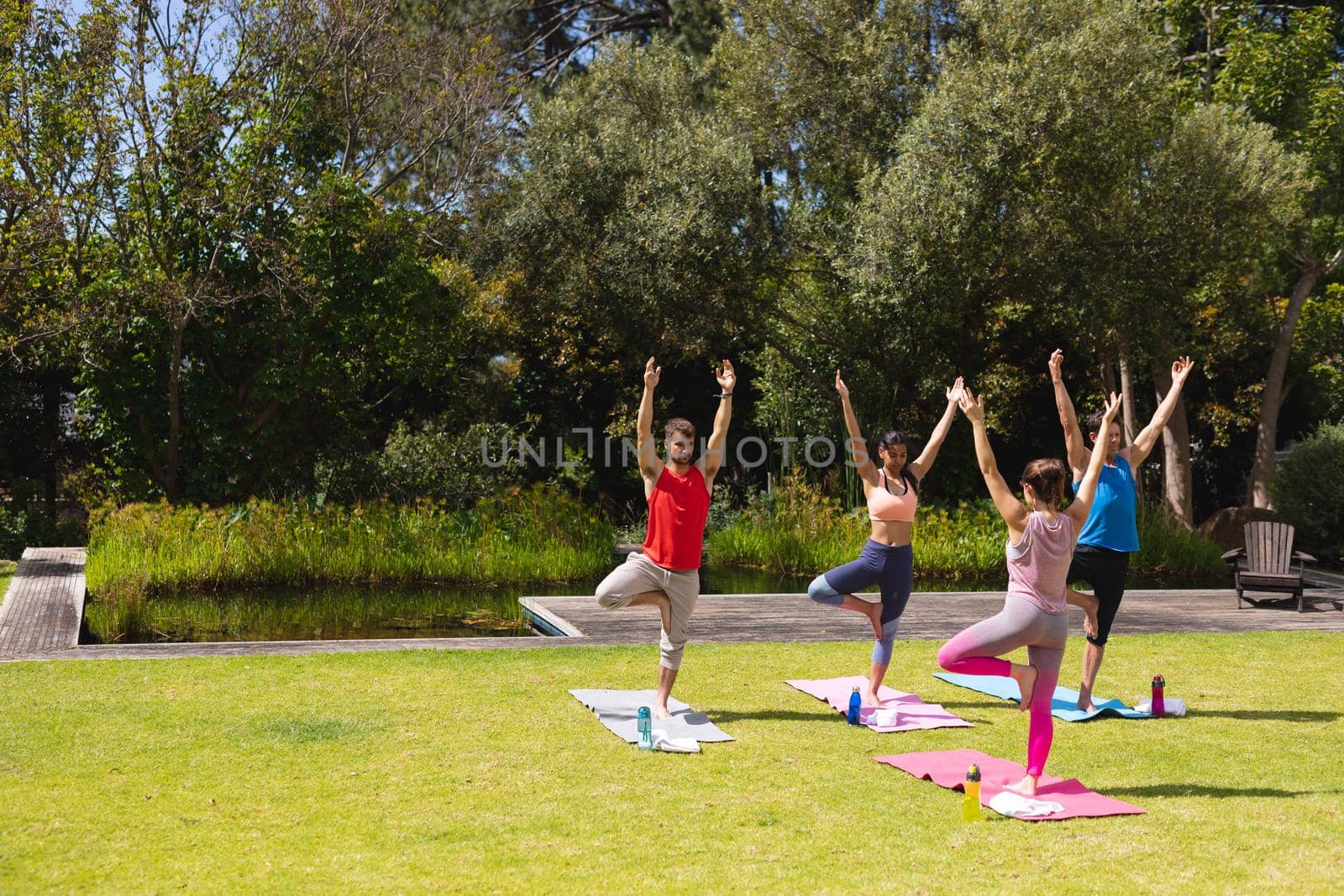 Female instructor teaching yoga to men and woman in public park on sunny day by Wavebreakmedia