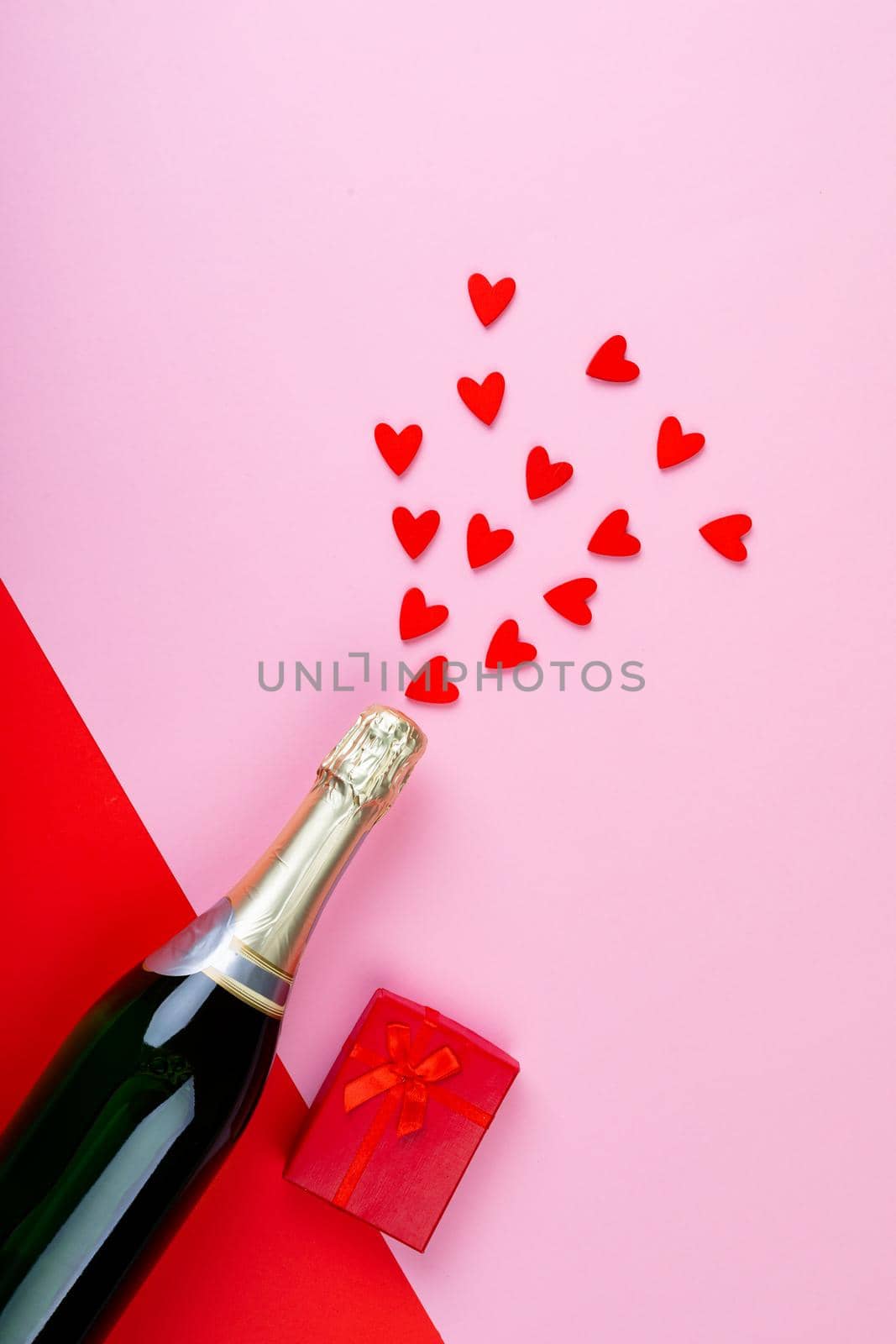 Champagne bottle splashing red heart shapes by gift box on pink background by Wavebreakmedia
