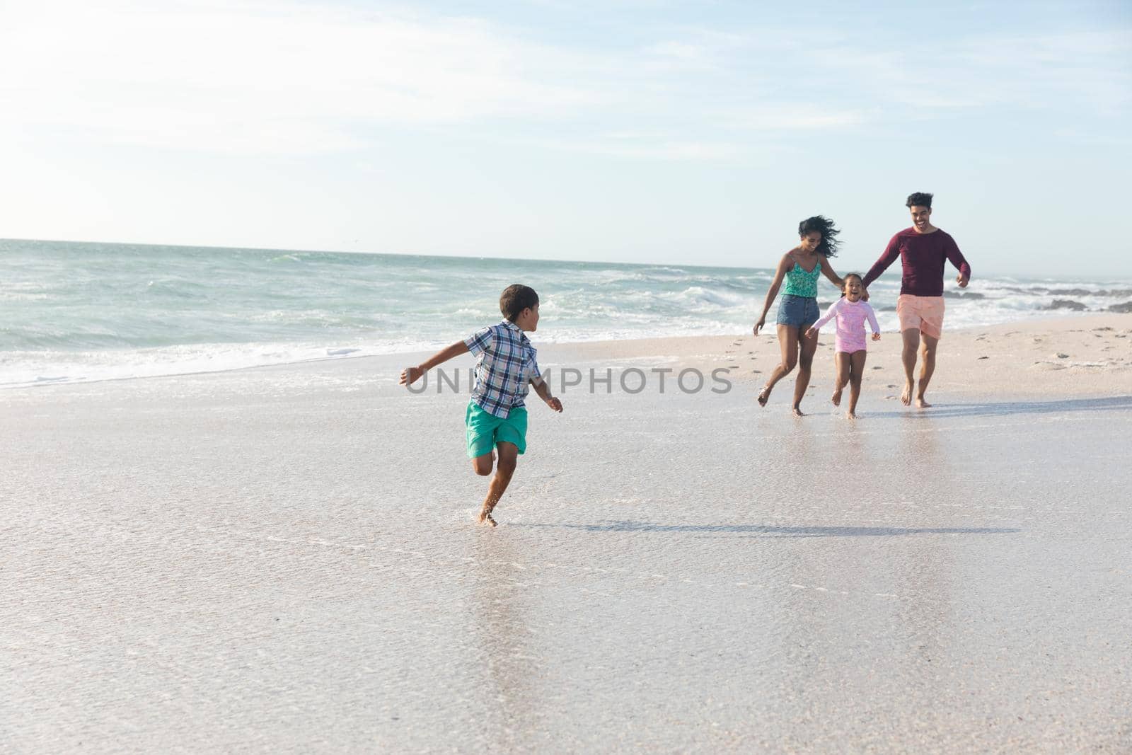Biracial boy running while looking back at family following him on shore during sunny day. lifestyle and weekend.