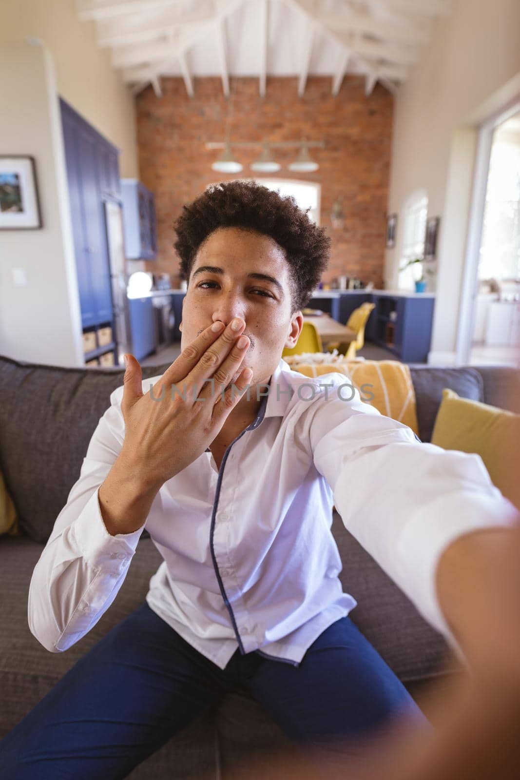 Portrait of biracial young man blowing air kiss on virtuality date at home. lifestyle and virtuality.