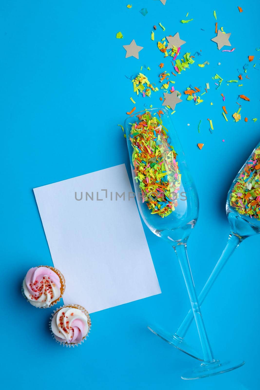 Champagne flutes with confetti by cupcakes and blank paper with copy space on blue background by Wavebreakmedia