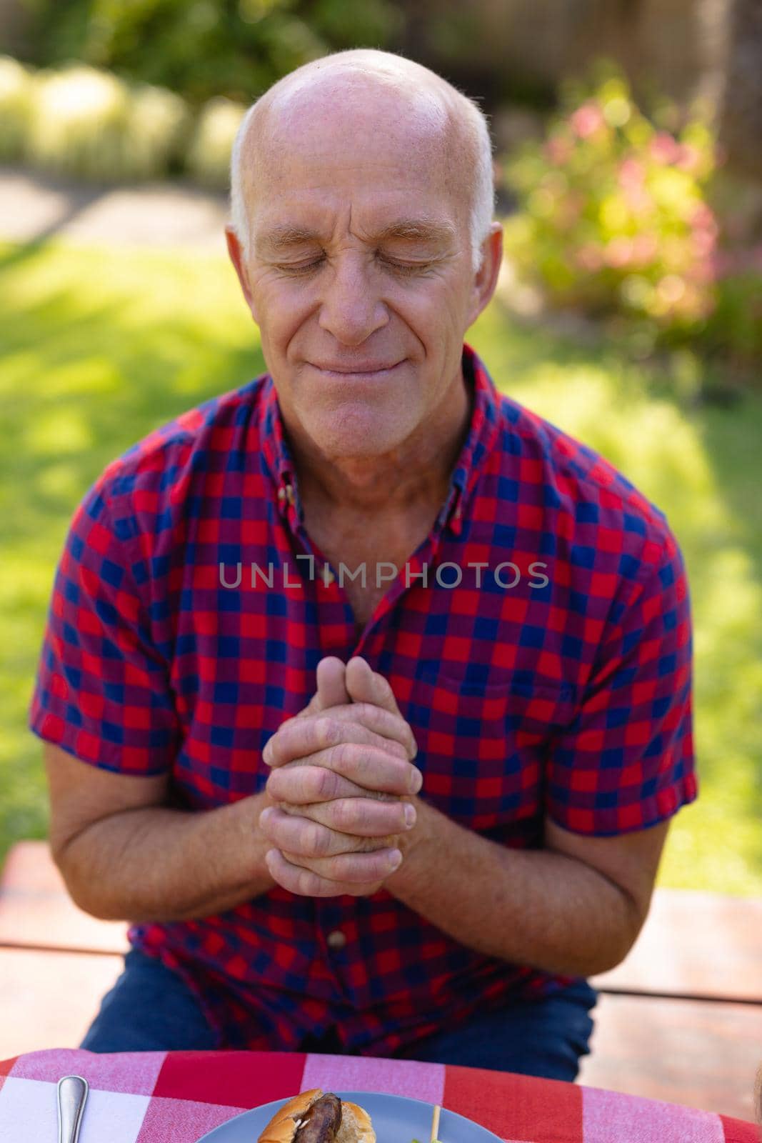 Caucasian senior man with eyes closed and hands clasped praying in garden. people and spirituality concept, unaltered.