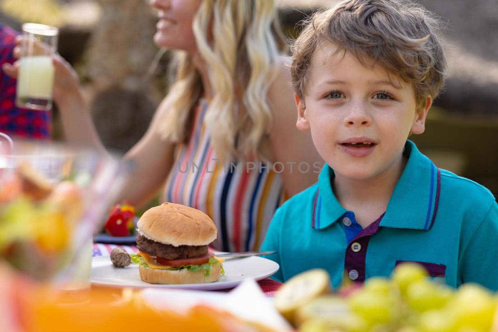 Portrait of caucasian boy sitting with family at table in the garden during lunch. family, togetherness and food concept, unaltered.