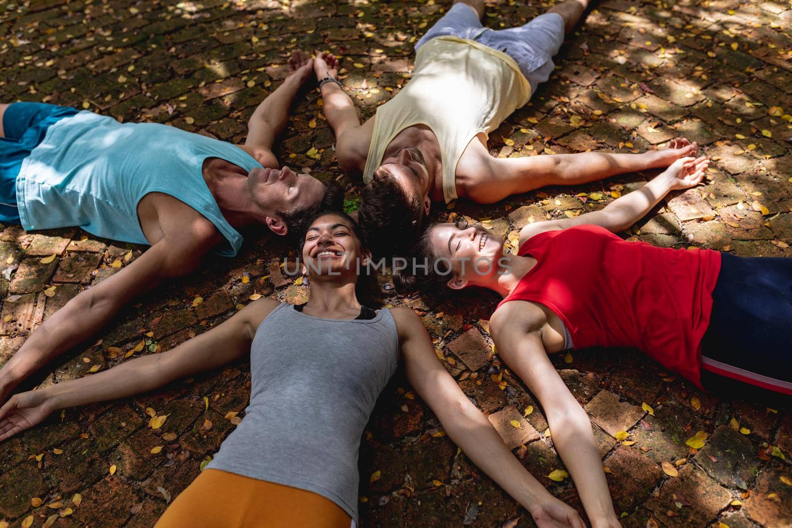 Smiling multiracial male and female friends relaxing together with arms outstretched on ground. yoga, healthy lifestyle and fitness.
