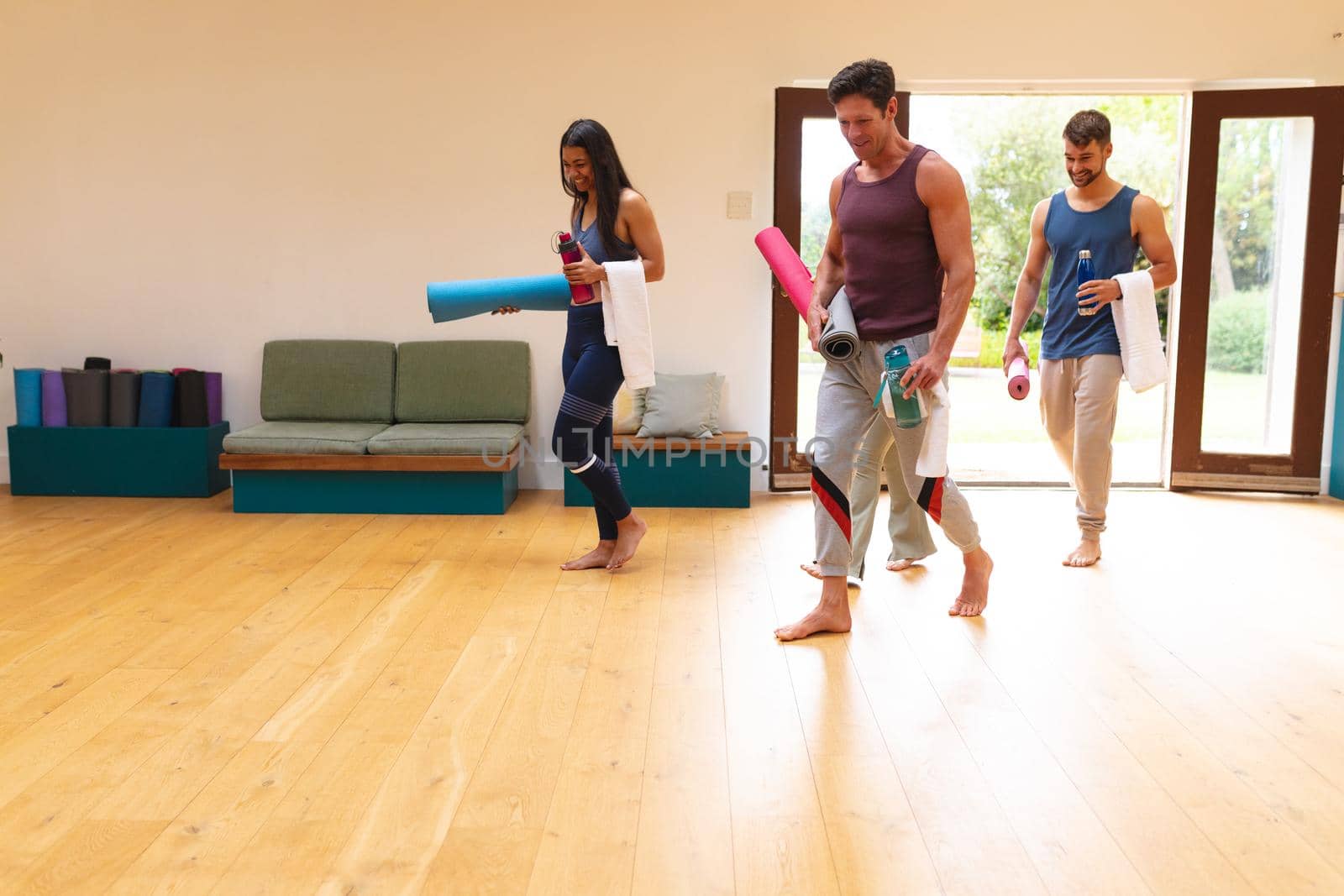 Multiracial men and women entering with exercise mats in yoga studio by Wavebreakmedia