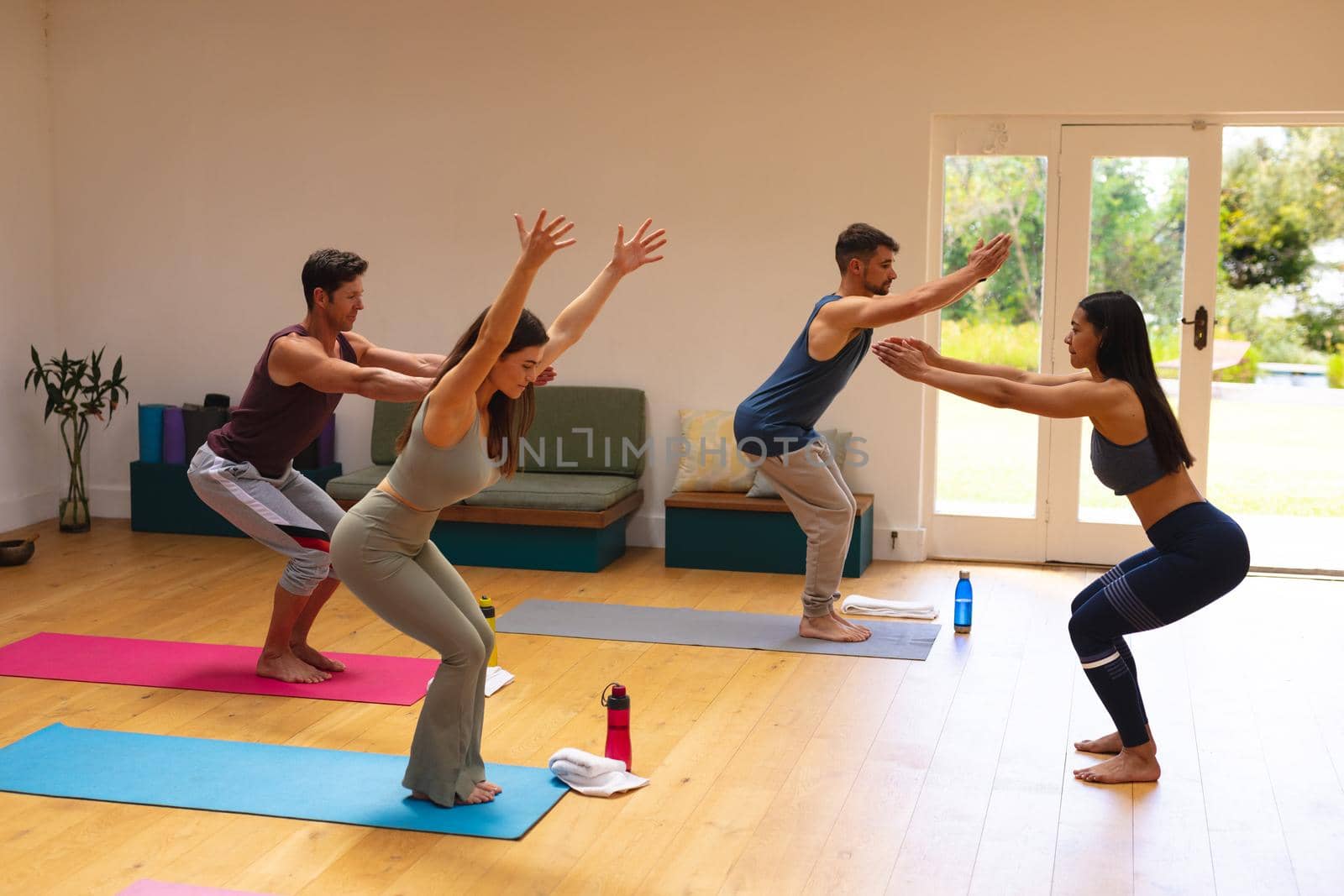 Slim female instructor assisting multiracial men and woman in practicing yoga pose at yoga studio. fitness, yoga and healthy lifestyle.