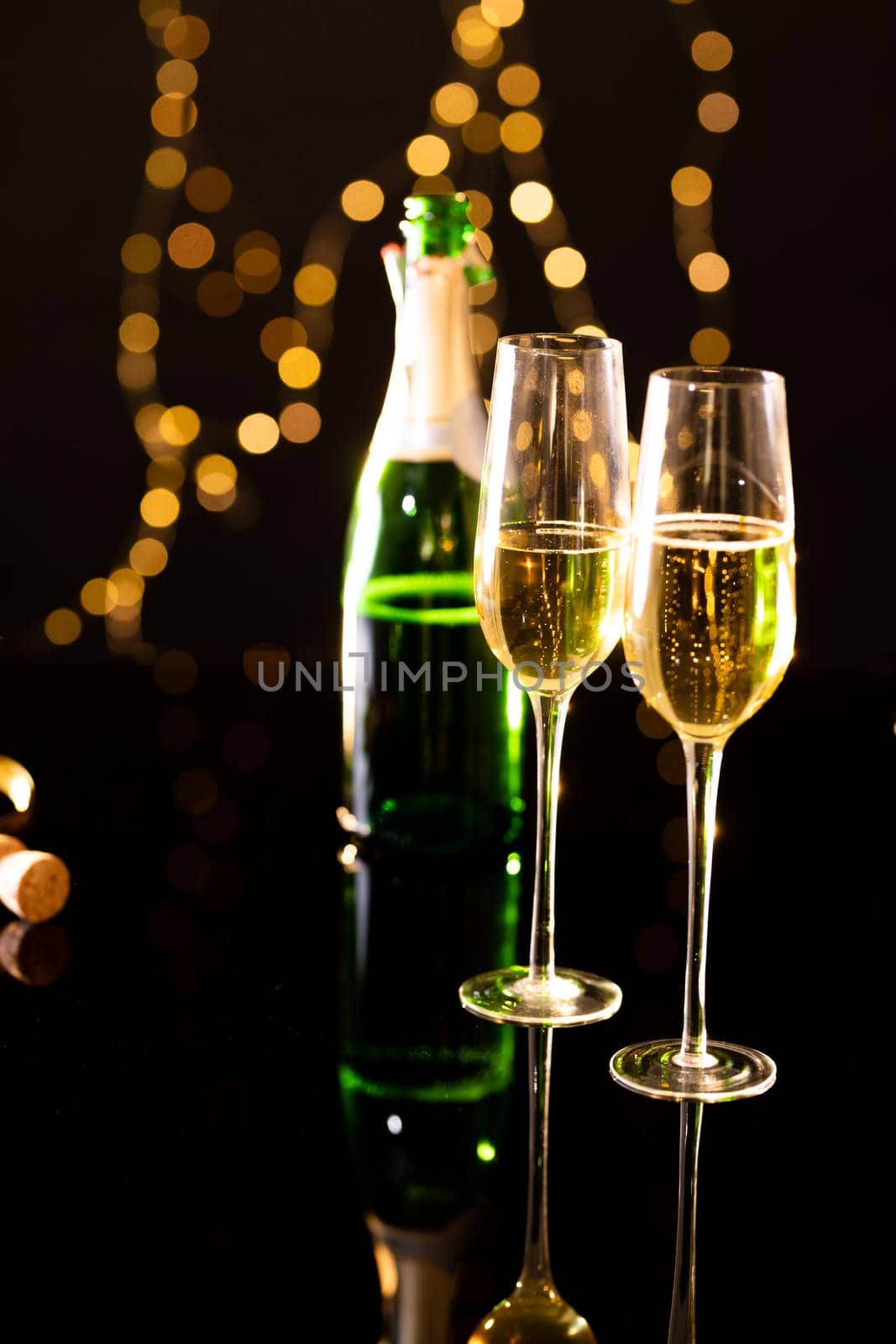 Close up of champagne in flutes with bottle reflecting on glass table. celebration and party with copy space.