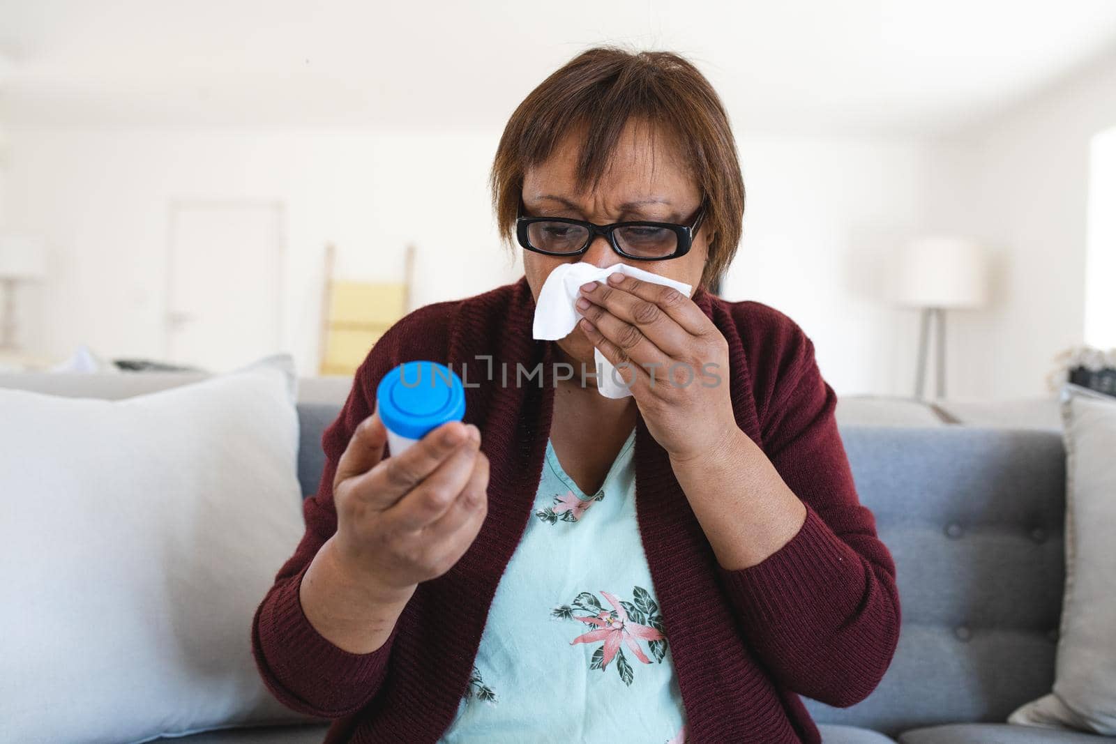 African american senior woman suffering with cold and flu holding medicine container at home by Wavebreakmedia