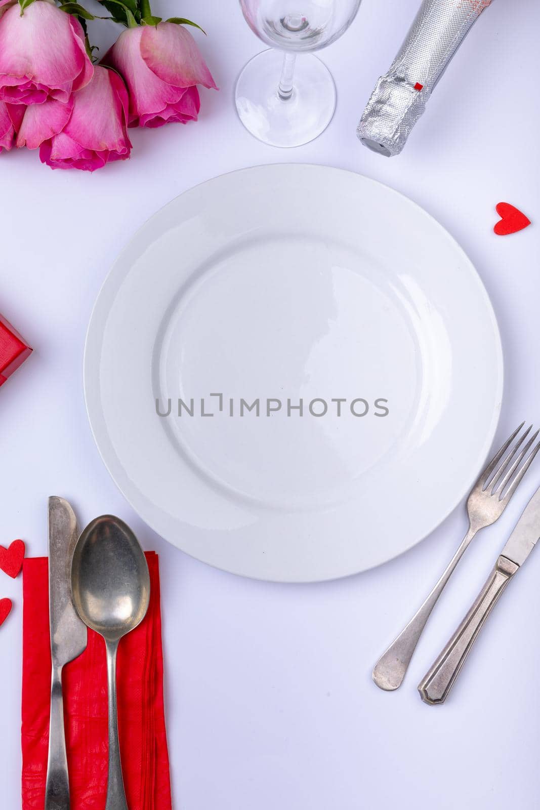 Empty white plate surrounded by pink roses with bottle and cutlery on table. love and valentine dining with copy space.