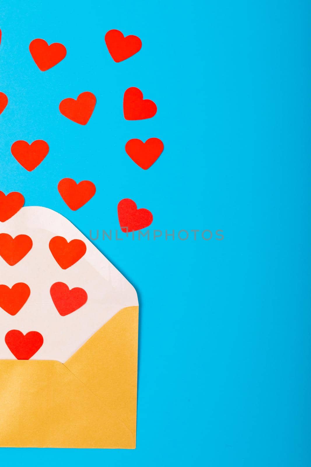 Overhead view of open beige envelope with red heart shapes by copy space on blue background. love and valentine present.