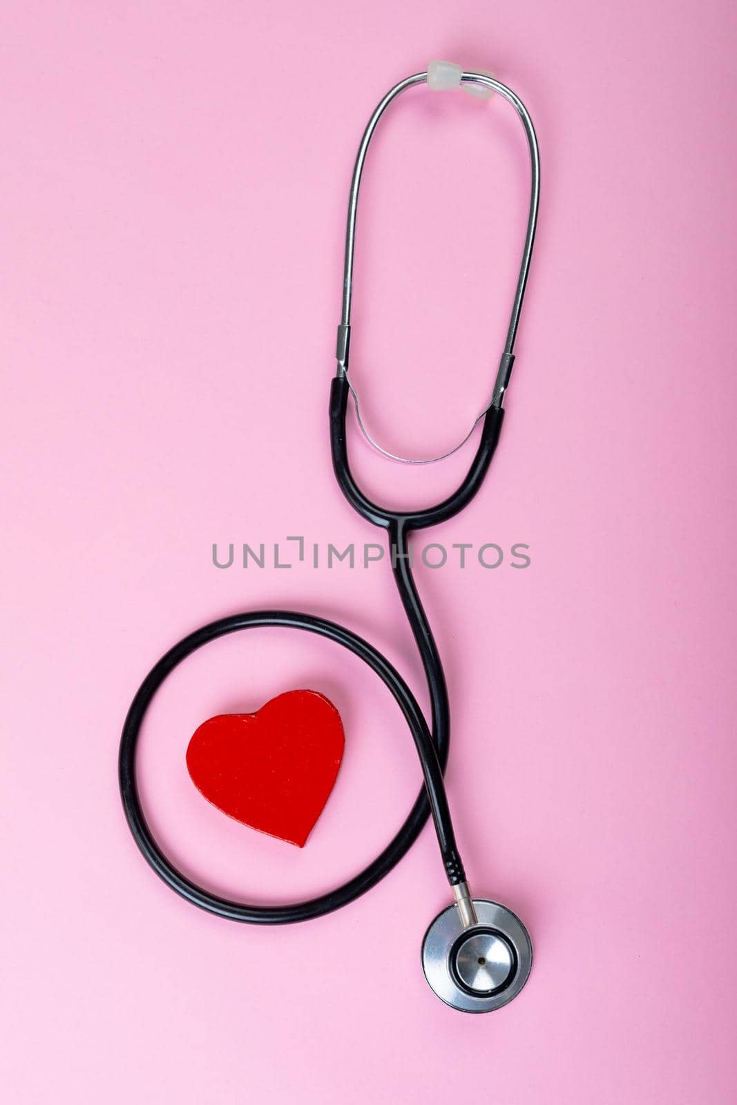 Overhead view of stethoscope around red heart shape on pink background with copy space. healthcare and valentine.
