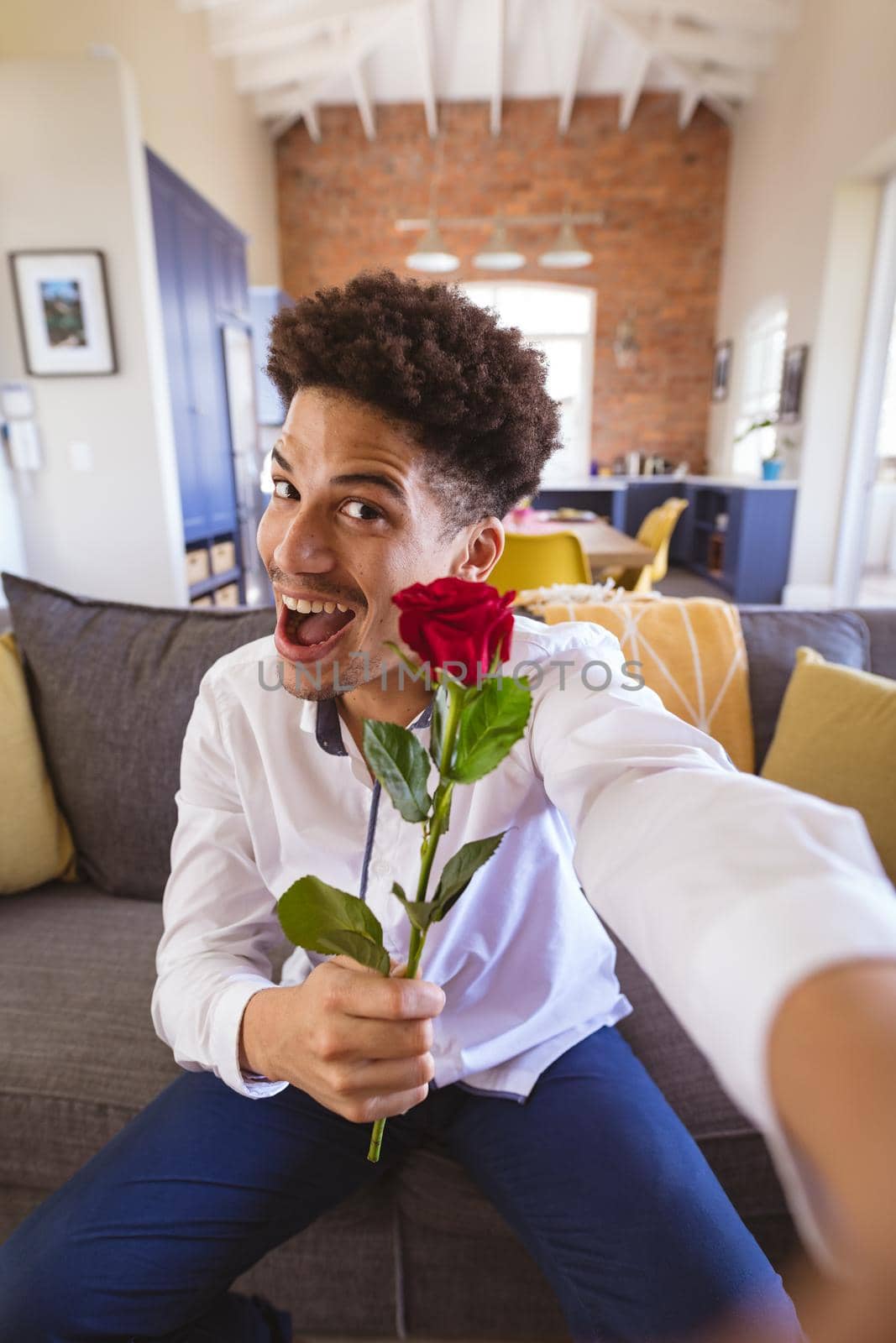 Portrait of biracial young man with rose enjoying virtual date at home. lifestyle and virtuality.