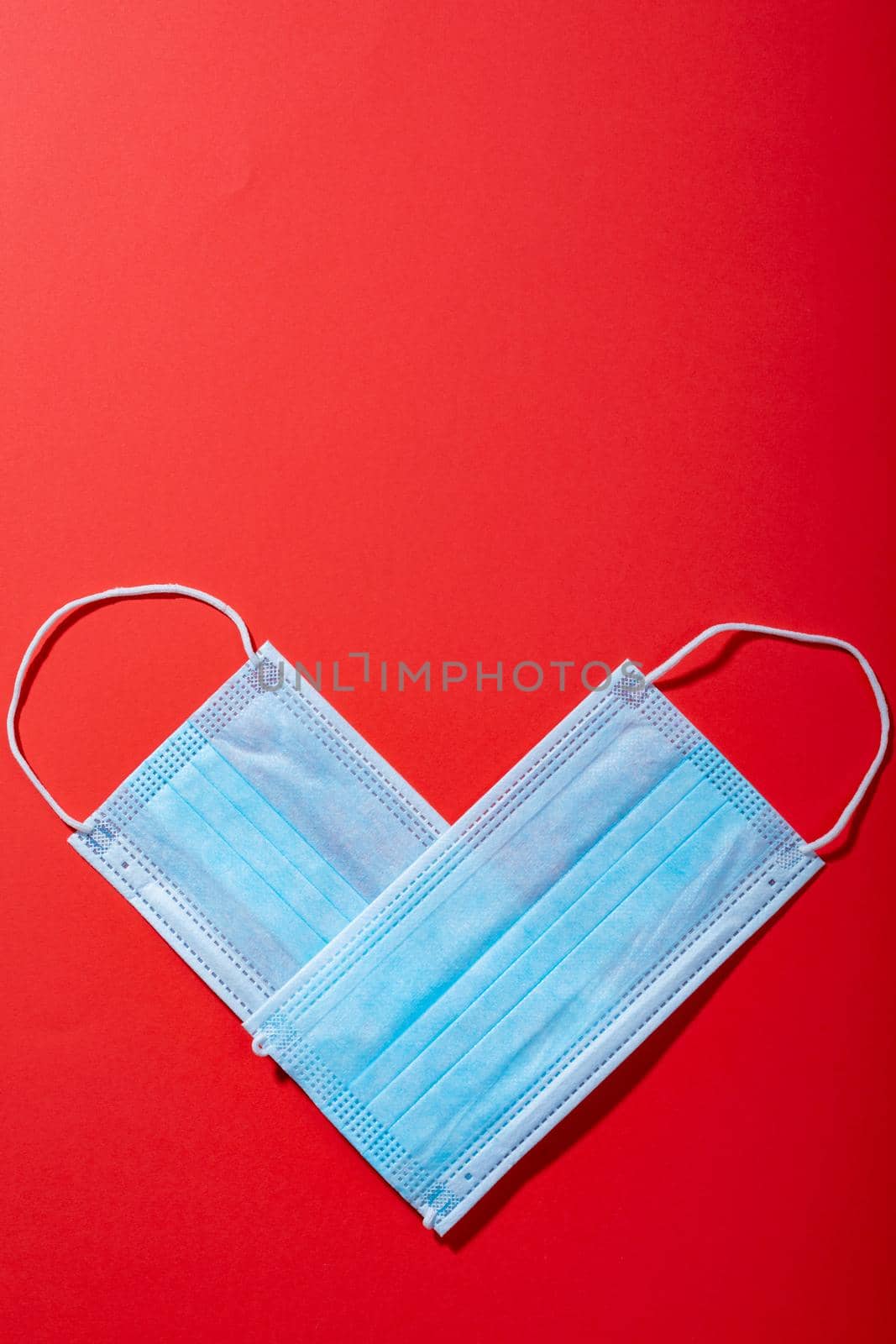 Overhead view of protective face masks arranged in heart shape on red background, copy space by Wavebreakmedia