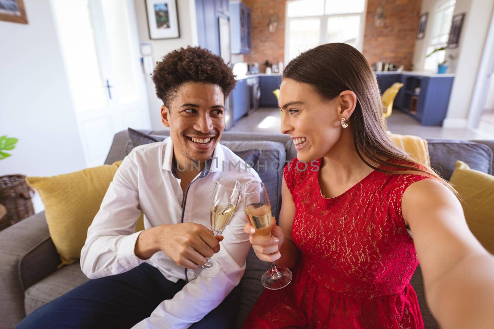Happy young biracial couple toasting champagne flutes while taking selfie at home. lifestyle, celebration and memories.