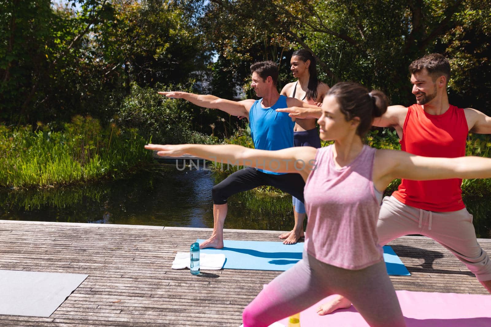 Female yoga instructor assisting men and woman during exercise session at park by Wavebreakmedia