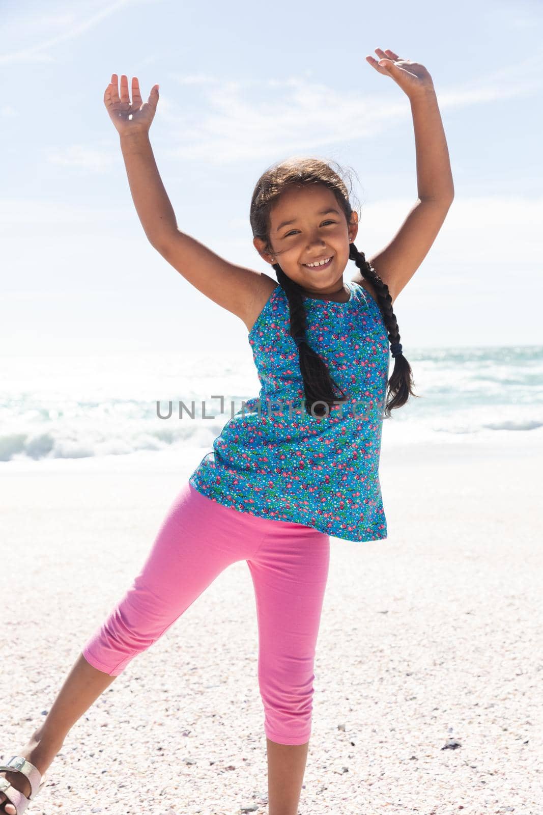 Full portrait of cheerful little biracial girl enjoying sunny day at beach against sky. childhood and weekend.