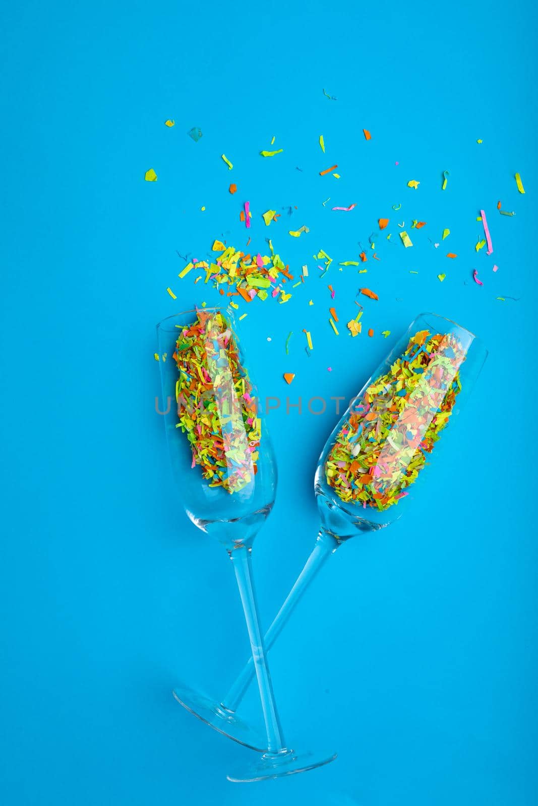 Overhead view of colorful confetti and champagne flutes isolated on blue background, copy space. valentine's day and love concept.