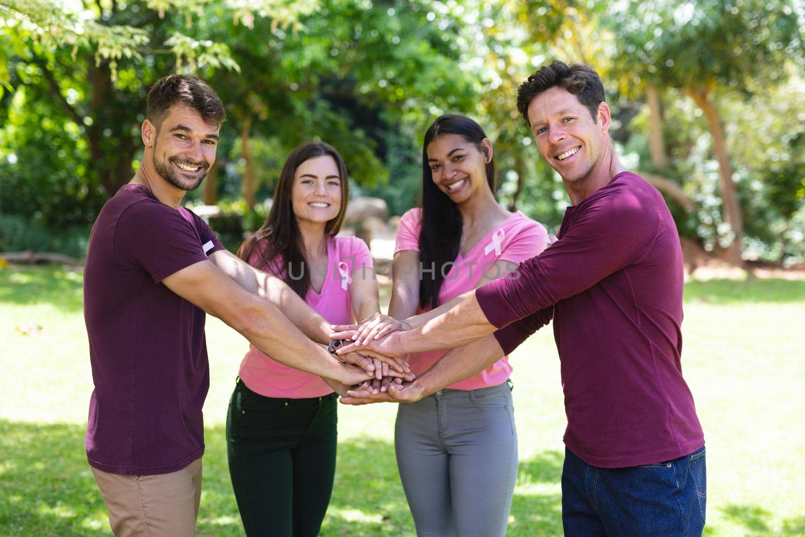 Portrait of happy multiracial friends stacking hands during breast cancer awareness campaign at park by Wavebreakmedia